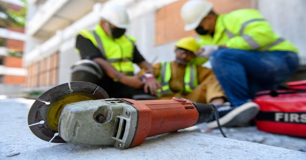 Constructions workers help an injured worker next to some equipment.