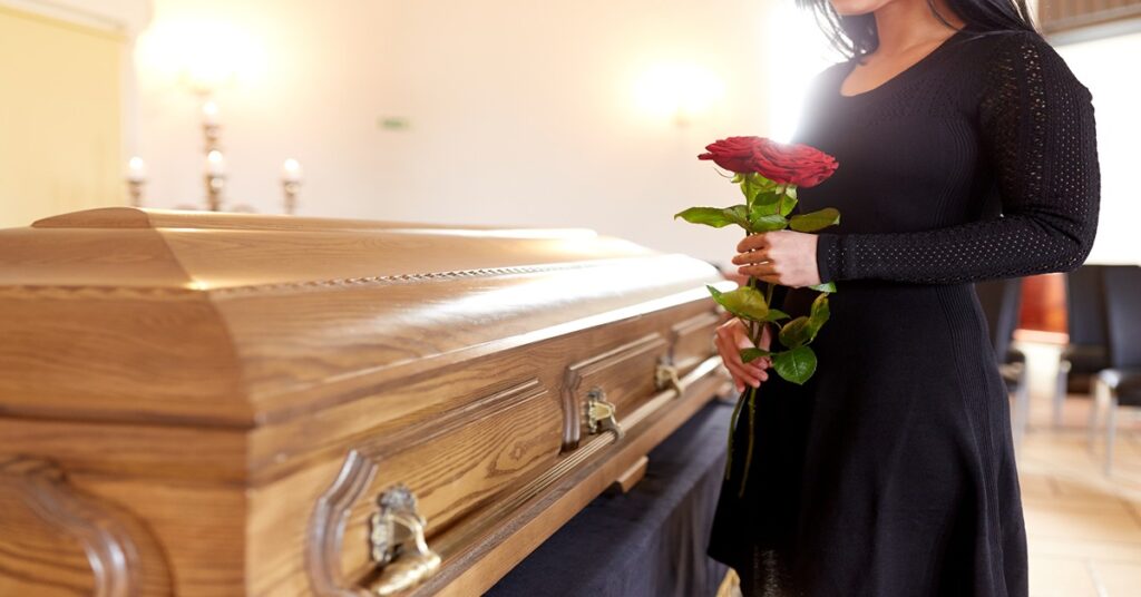 Mourner holding flowers as she grieves next to a funeral casket.