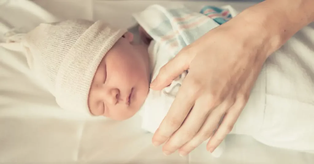 A newborn baby lying asleep as a parent's hand cradles it