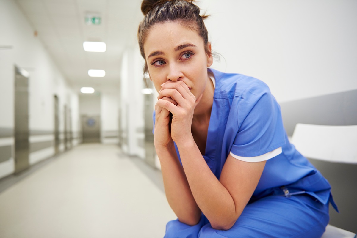 Worried female nurse sitting in a hospital hallway eyes red with tears