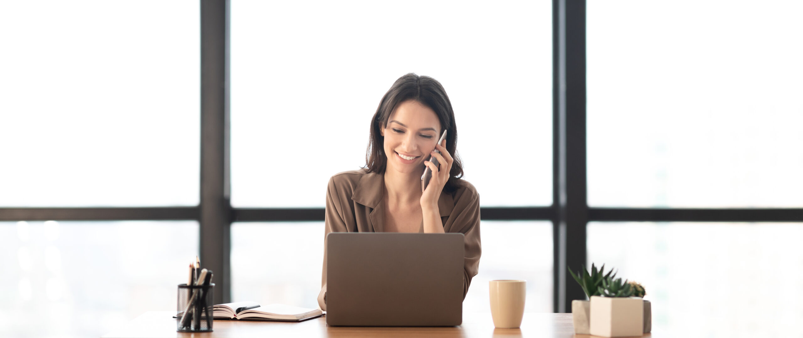 Woman talking happily on the phone as she looks at her laptop