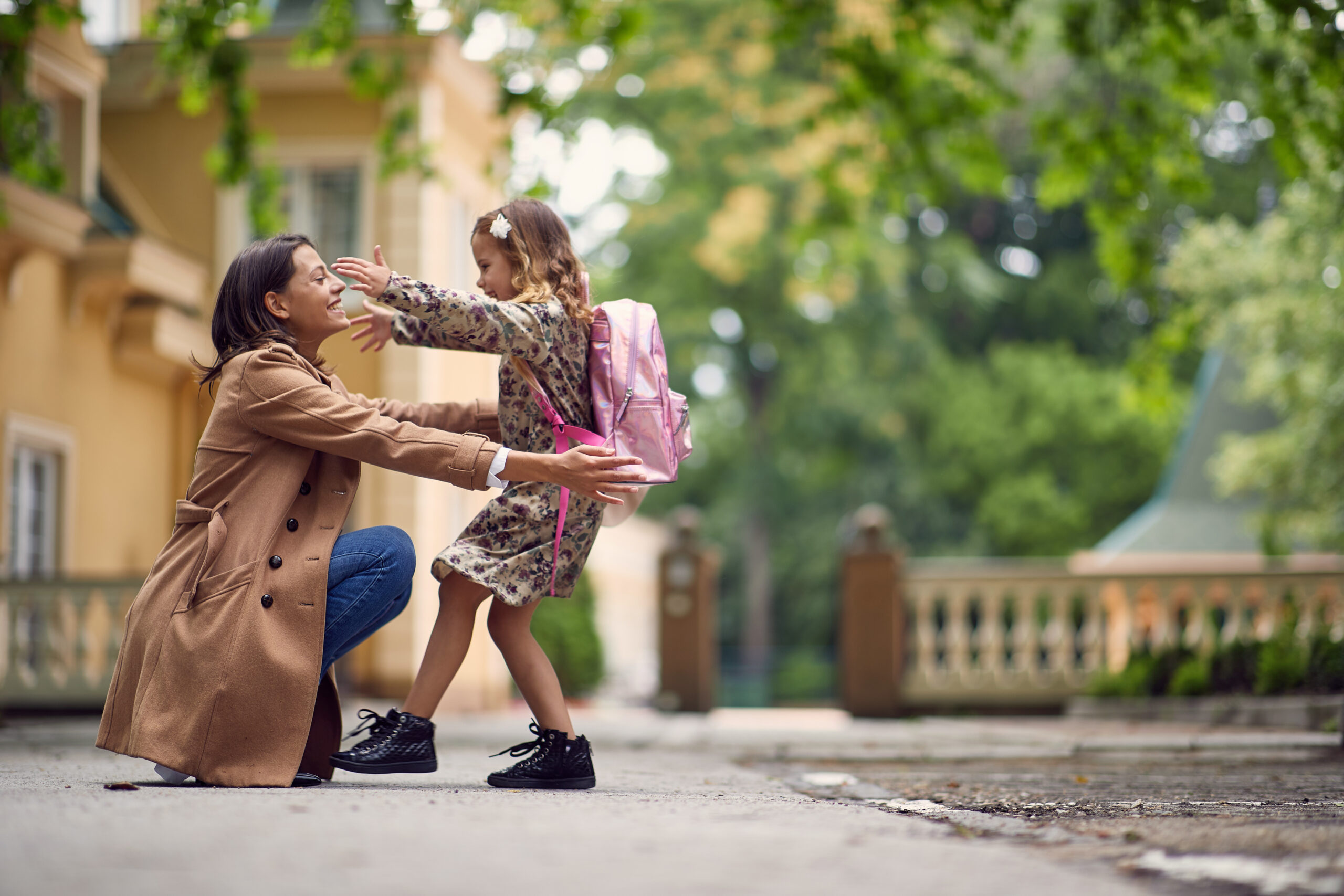 Young woman kneeling down to hug her daughter as she picks her up from school