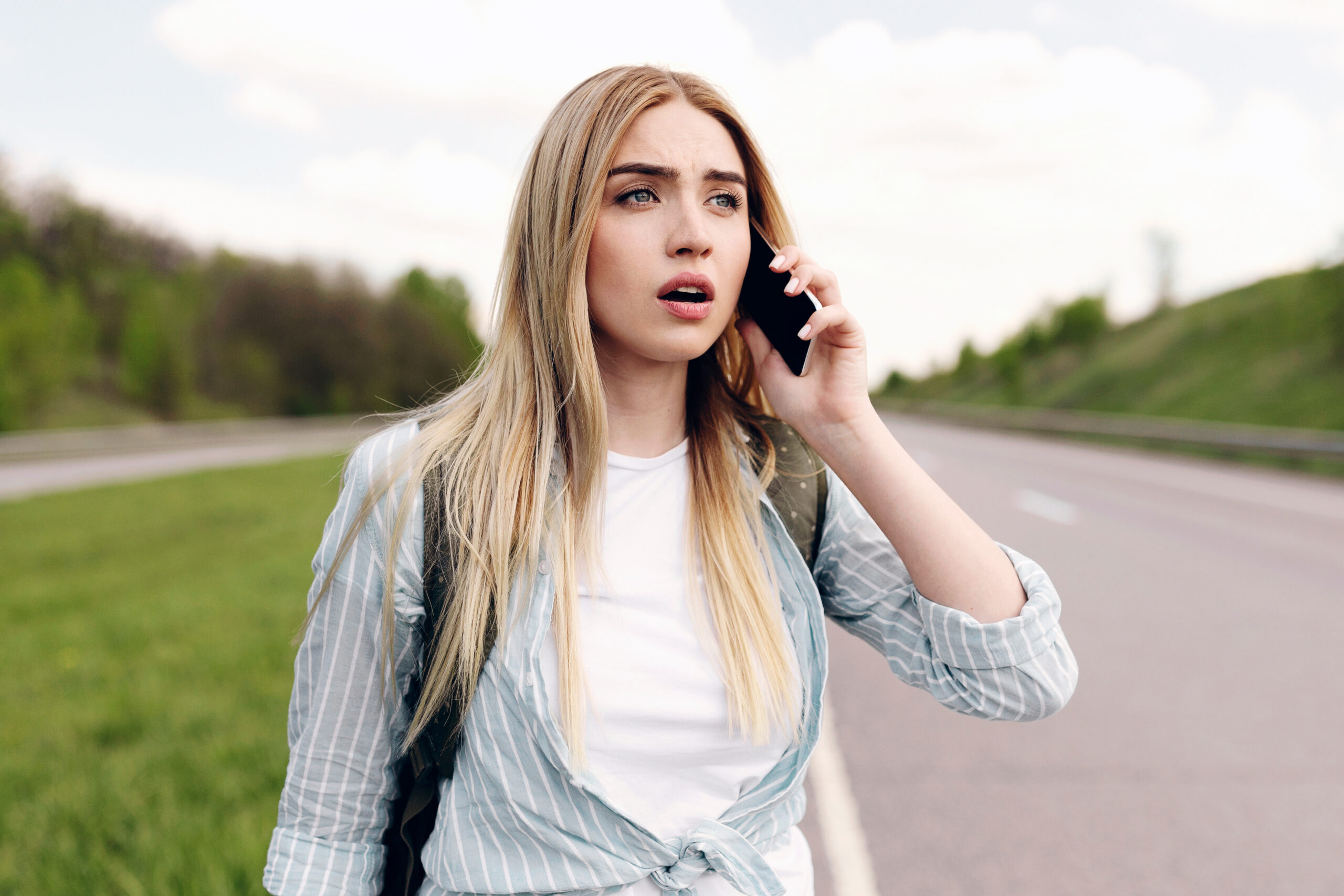 Lost confused woman talking on the phone while walking down the highway