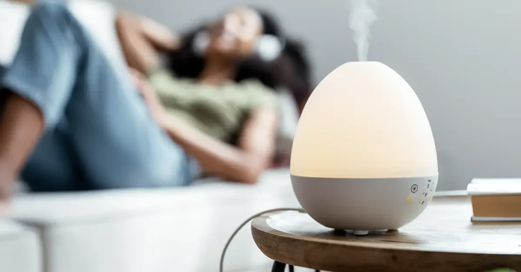 image of a woman relaxing on couch with an air diffuser in the foreground on a table