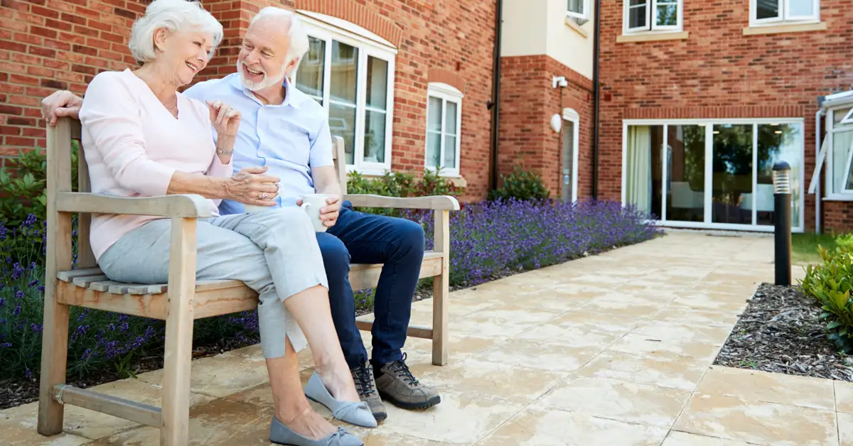 image of elderly couple outside on bench at retirment home