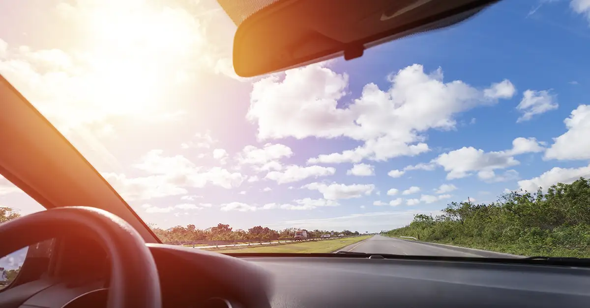image looking out the windshield of a car to the road and a bright cloudy sky